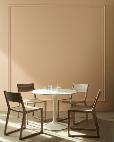 An Autumn Leaf-painted dining room with white cuckoo clock, wood chairs, and modern white table with a house plant.