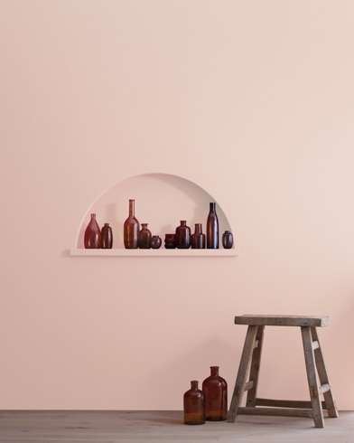 A wood stool and bottles in front of a Pale Petal-painted wall with inset shelving holding a variety of empty bottles.