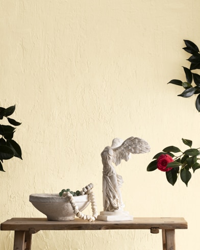 A statue and a bowl on a wooden bench in front of a textured wall painted in Ivory Lustre.