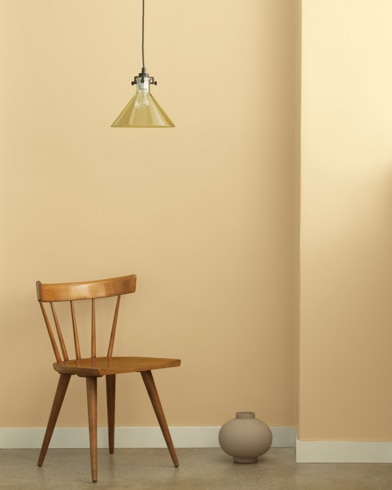 A single-bulb light hangs over a wooden chair and small ceramic pot in front of a wall painted Desert Tan.