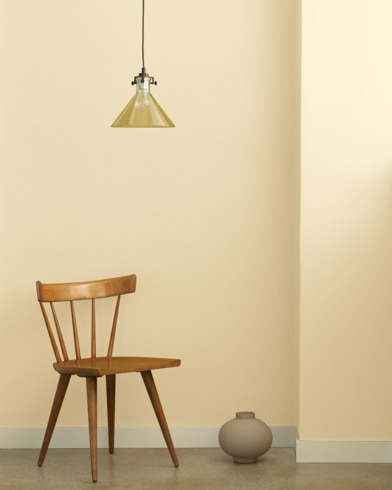 A single-bulb light hangs over a wooden chair and small ceramic pot in front of a wall painted Rich Cream.
