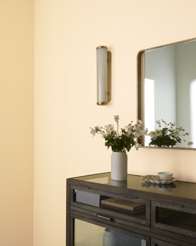 A brown table topped with a tea set and vase of flowers stands under a mirror hanging on a wall painted Lion Yellow.