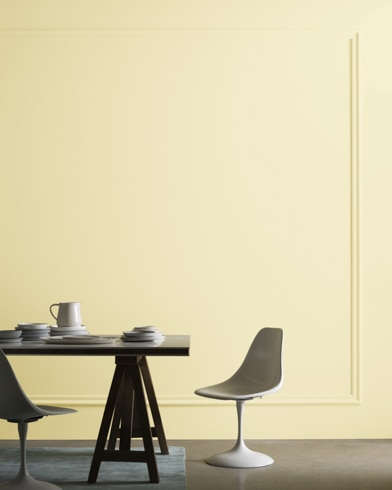 A midcentury modern dining table with two chairs sits in front of a wall painted North Star.