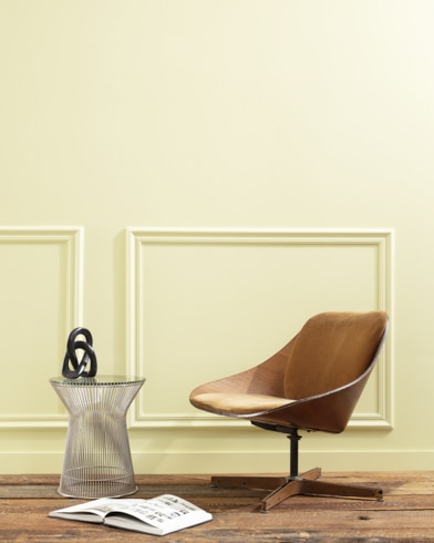 A flat wood riser holds a curved wooden chair, glass vase and open book in front of a paneled wall painted Hawthorne Green.