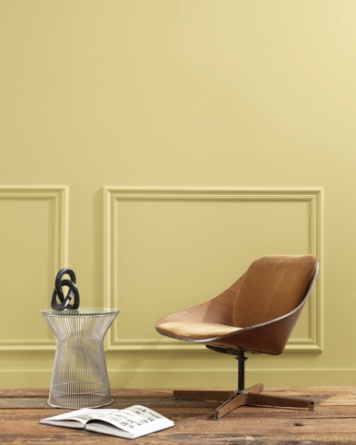 A flat wood riser holds a curved wooden chair, glass vase and open book in front of a paneled wall painted Artichoke Hearts.