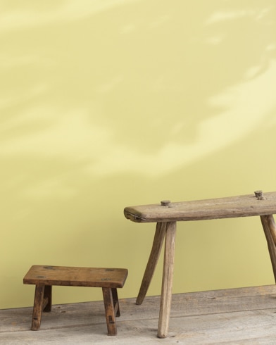 Two wooden stools, one large and one small, appear in front of a wall painted Sweet Pear.