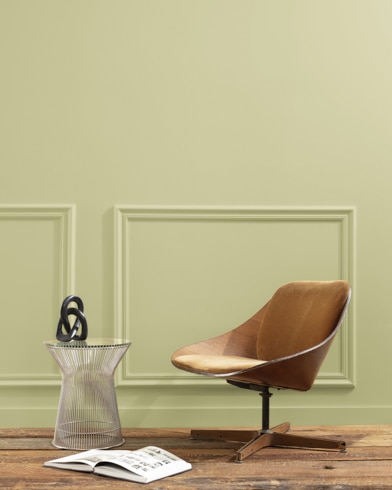 A flat wood riser holds a curved wooden chair, glass vase and open book in front of a paneled wall painted Grasshopper.