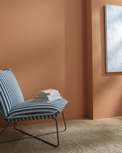 A Potters Clay-painted wall behind a striped armless lounge chair with books on