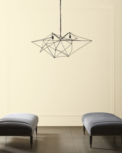 A modern, wiry chandelier hangs over two velvet ottomans in front of a wall painted Knitted Cape.