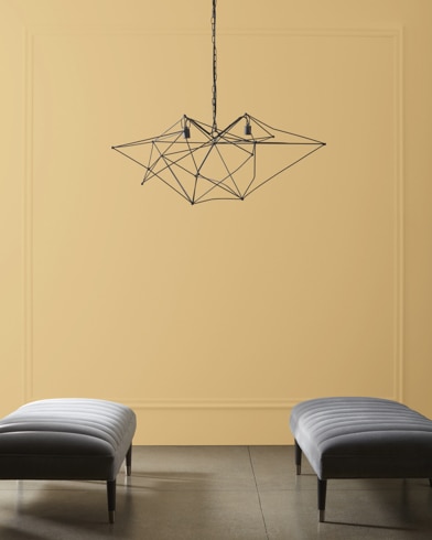 A modern, wiry chandelier hangs over two velvet ottomans in front of a wall painted Walk on the Beach¬Æ.